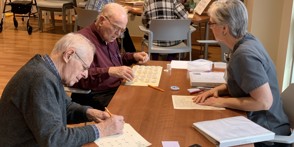 Two elderly men complete worksheets at a table