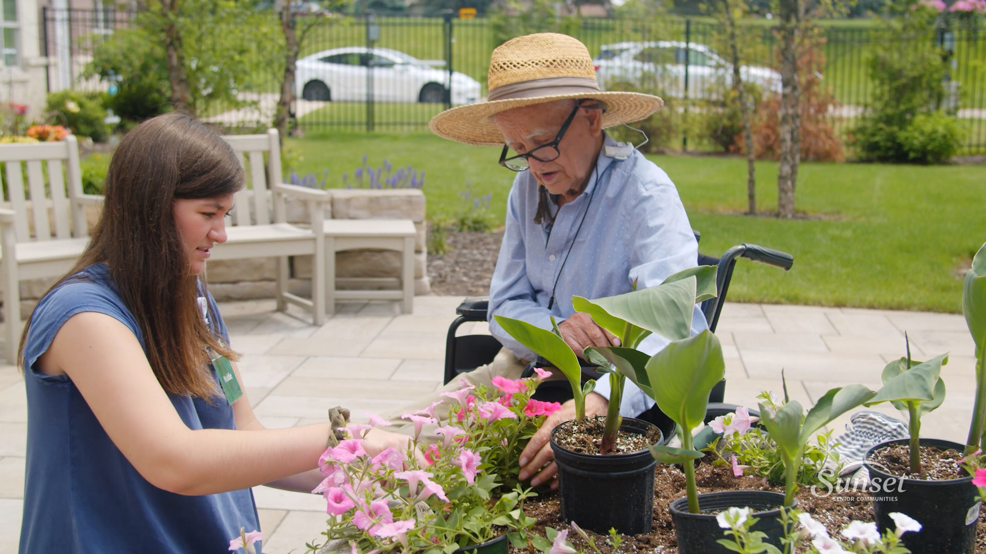 Sunset staff member helps a memory care resident plant flowers in a big planter